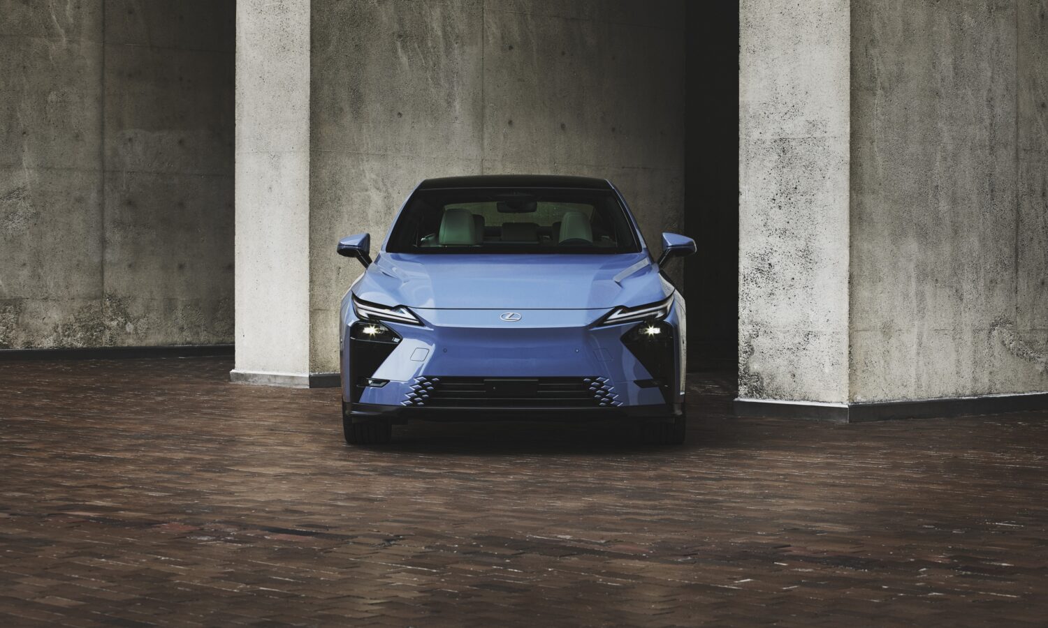 Lexus ES 350e in pale blue, head-on between concrete columns on brick paving