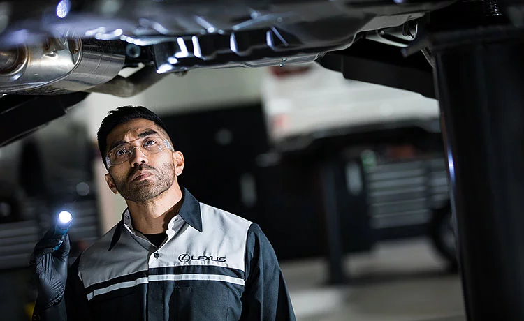 Lexus technician inspecting the underside of a car on the lift by torchlight