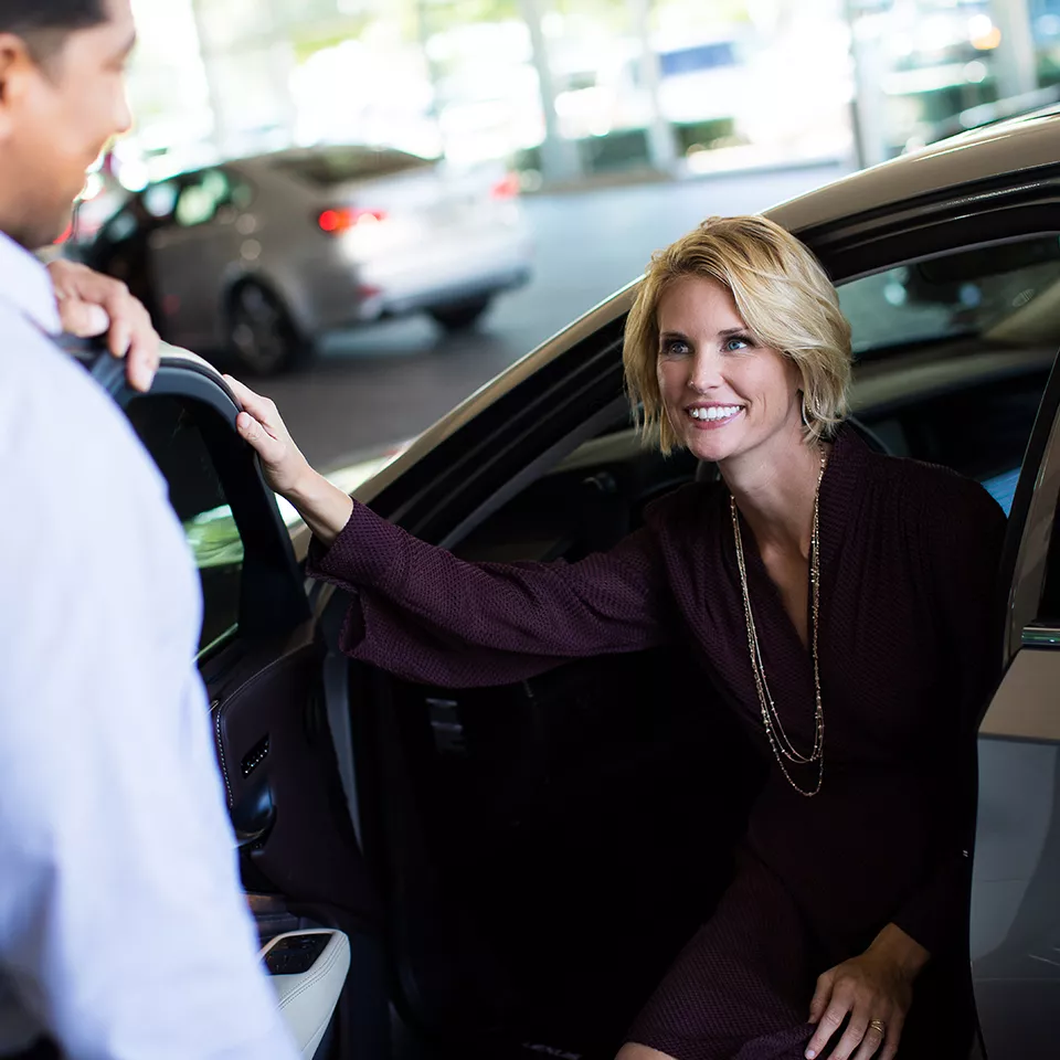 Lexus service advisor greeting a customer stepping out of her car at the drive-in bay