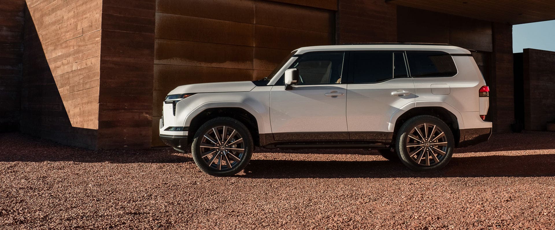 Lexus GX in white, side profile against a weathered corten wall