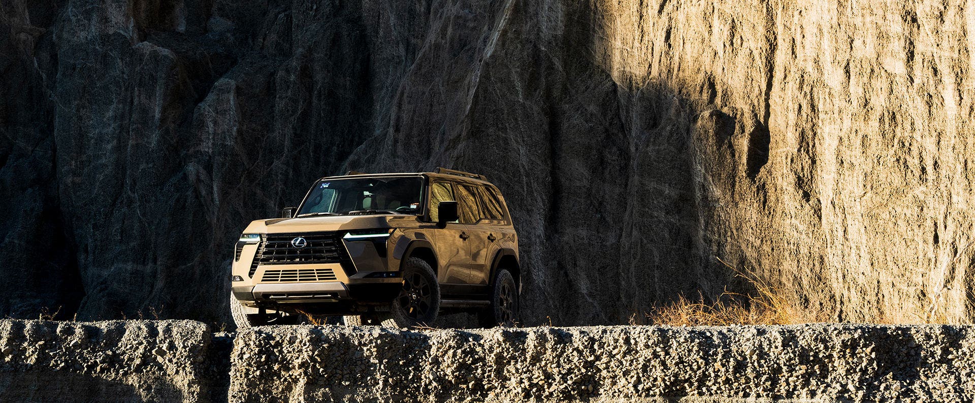 Lexus GX in bronze picking its way along a rocky ledge below a cliff face