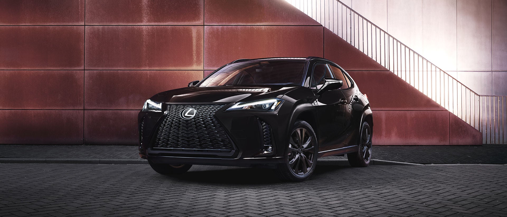 Lexus UX with the Appearance Package in black, parked against a corten steel wall