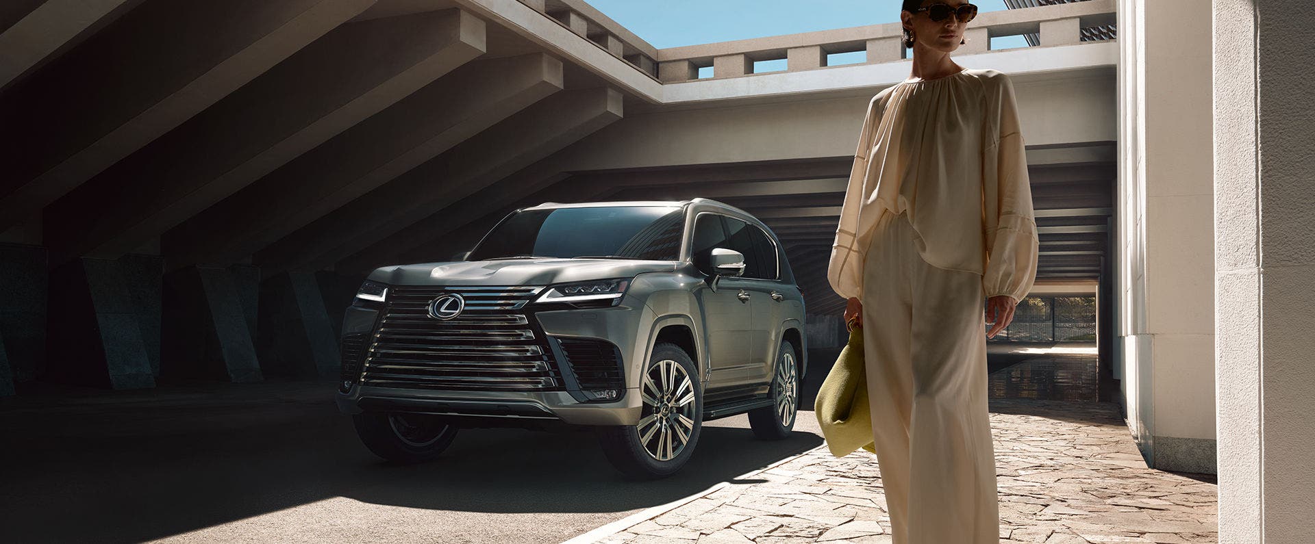 Lexus LX in dark gray beneath a concrete portico as a woman walks past