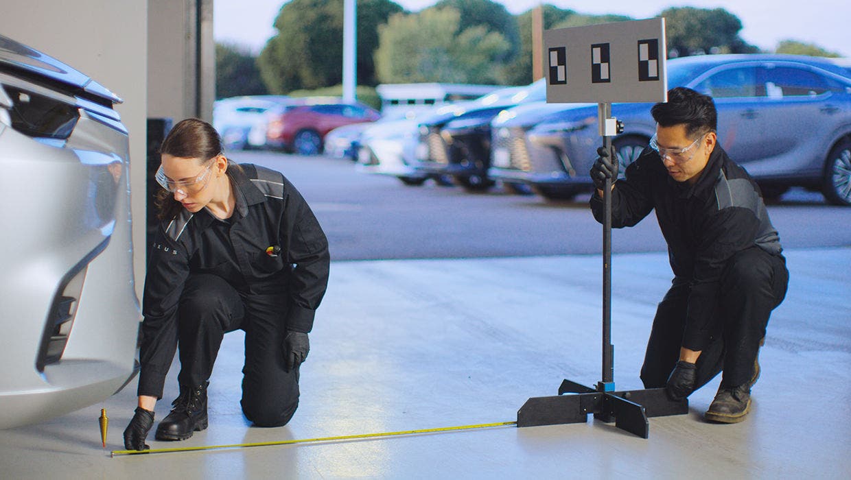 Two Lexus technicians setting up alignment equipment beside a car in the service lane