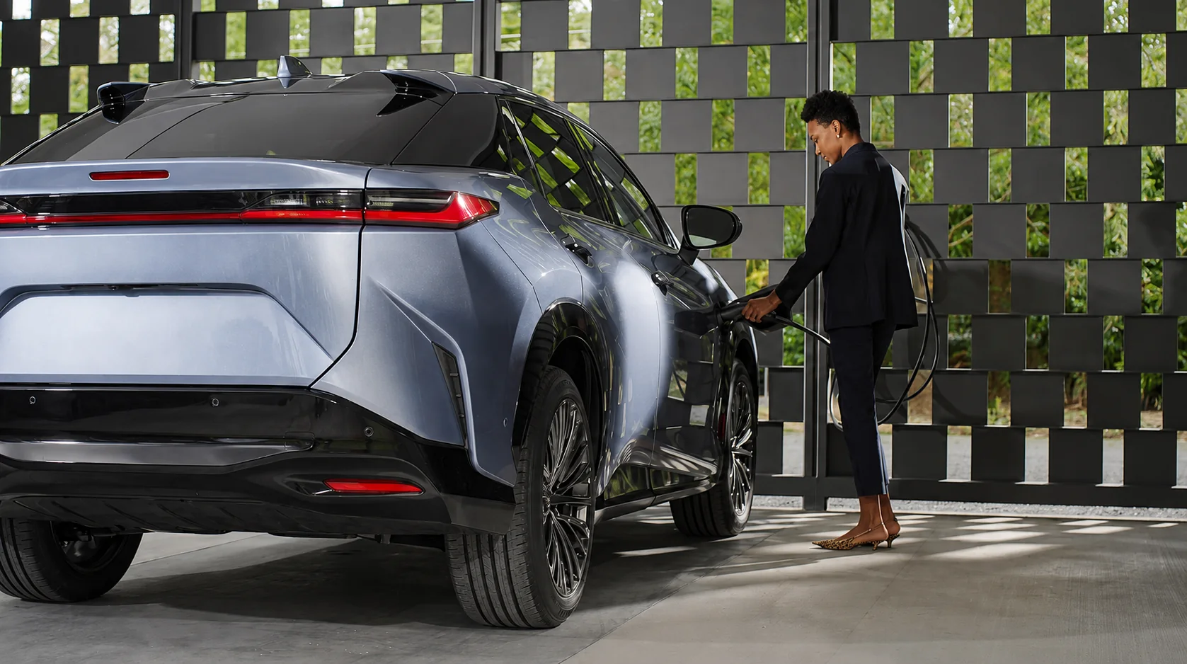 Lexus RZ owner plugging a charging cable into the car beside a slatted screen wall