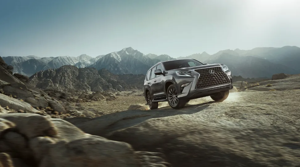 A gray Lexus GX driving on a rocky ridge with mountains behind
