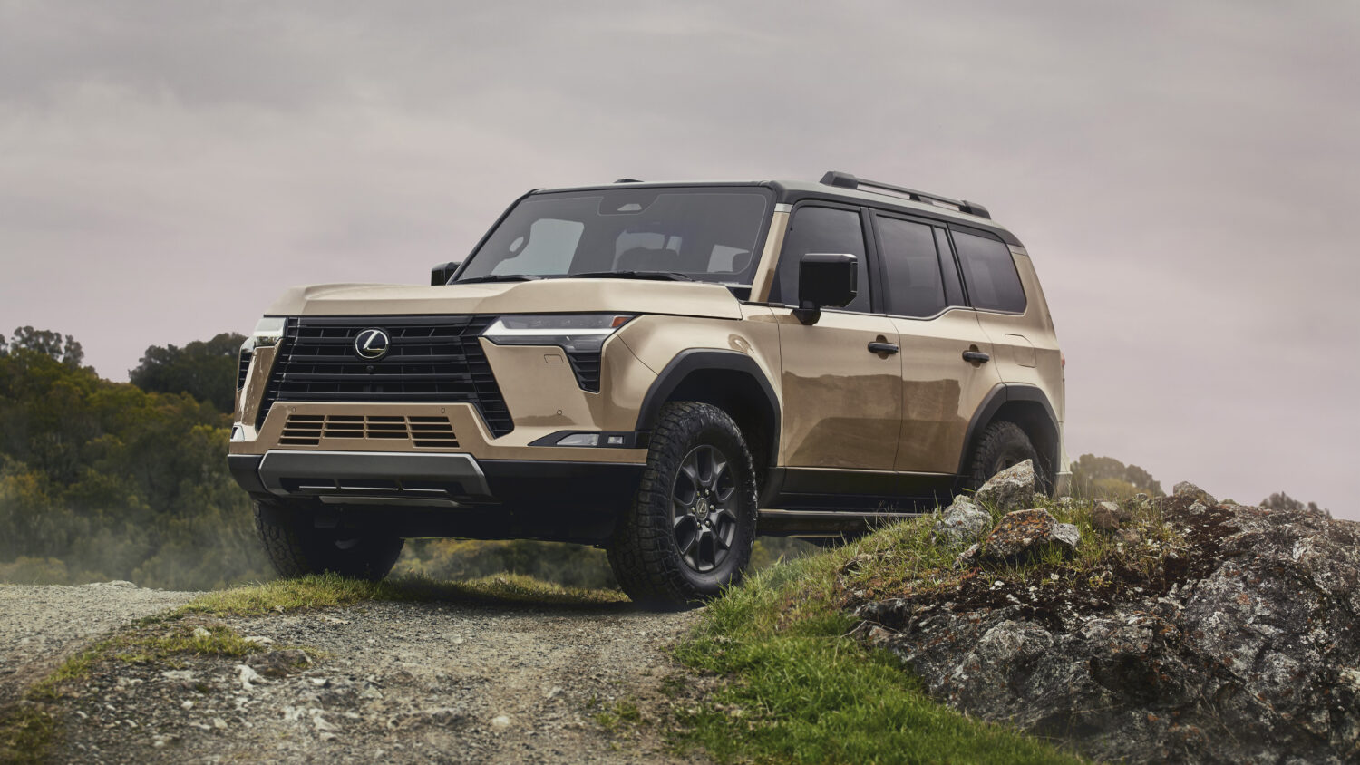 A sand-colored Lexus GX Overtrail on a rocky outcrop, front three-quarter view, low angle