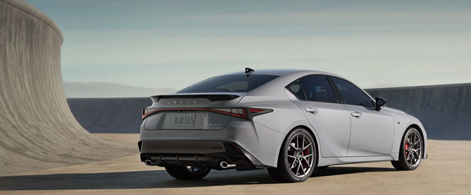 A gray Lexus IS sedan, rear three-quarter view, against a curved concrete wall