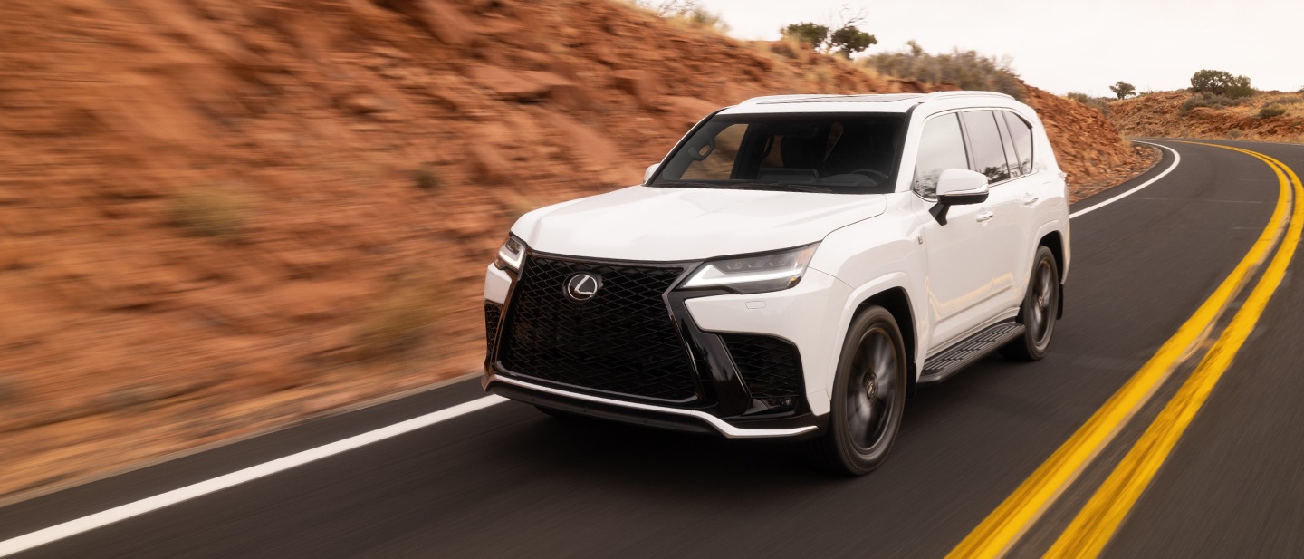 A white Lexus LX F SPORT on a highway curve below a red rock cutting