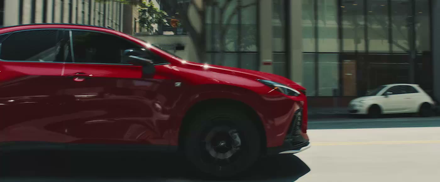 A red Lexus NX F SPORT driving through a city, seen in side profile