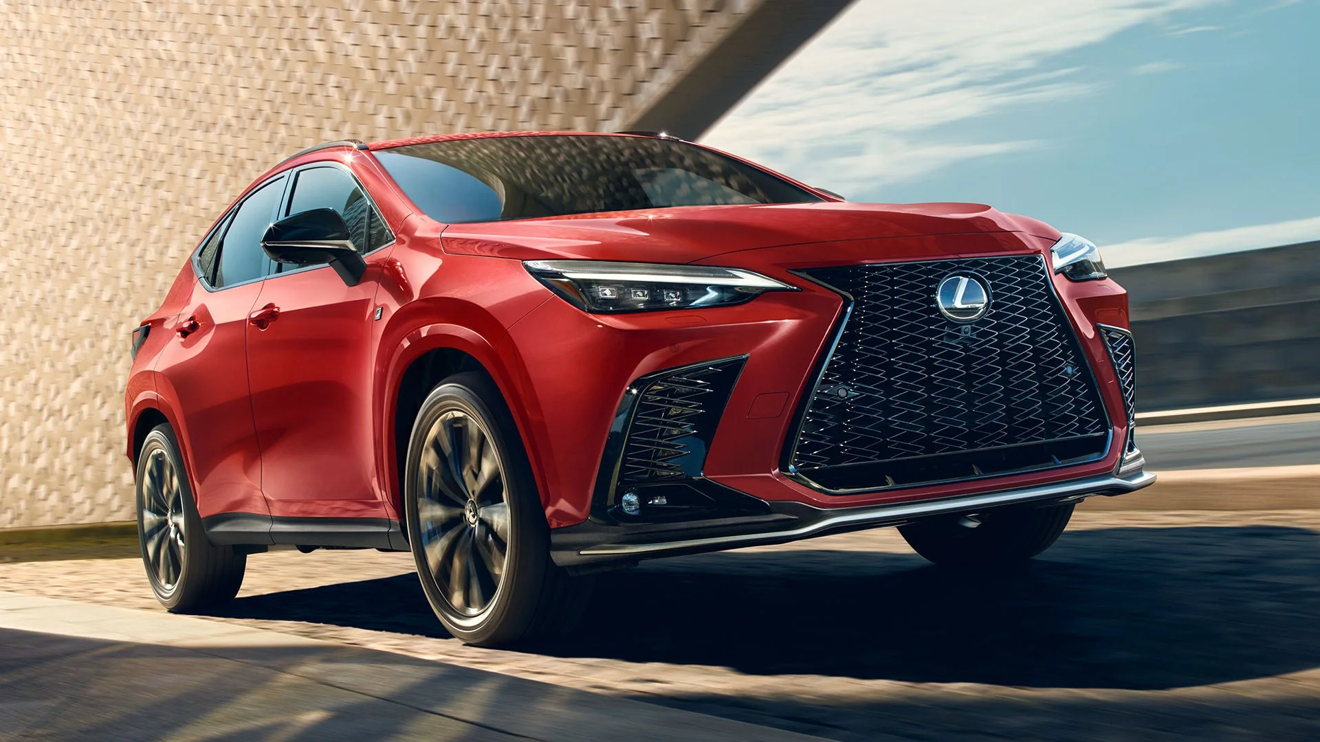A red Lexus NX F SPORT, front three-quarter view, with its spindle grille in sunlight