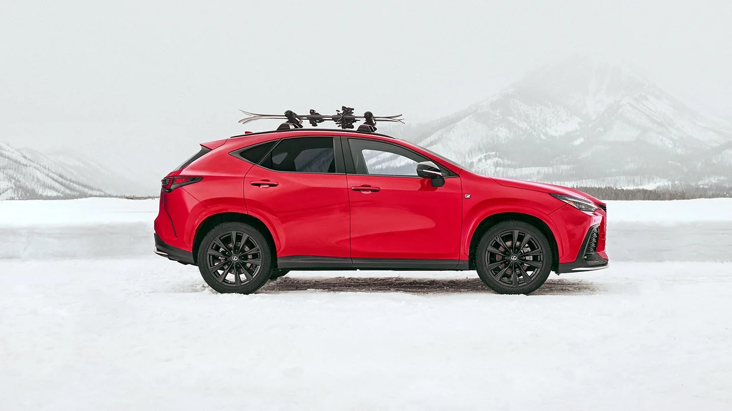 A red Lexus NX with a ski rack on the roof, parked side-on in a snowy field below mountains