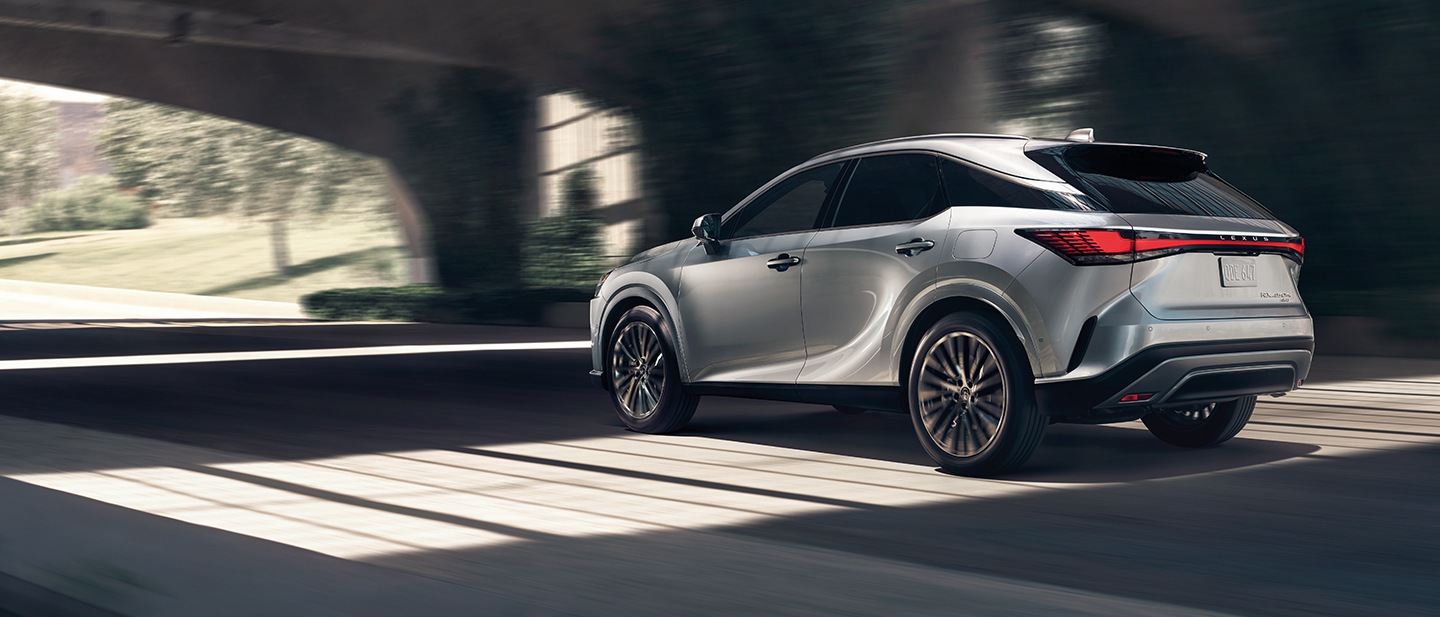 A silver Lexus RX hybrid in side profile, driving through the shadows under an overpass