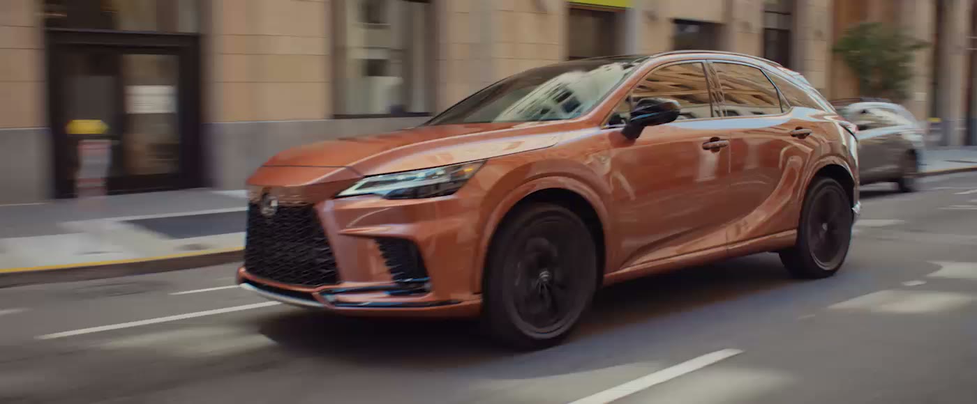 A copper Lexus RX driving on a city street, seen from the side