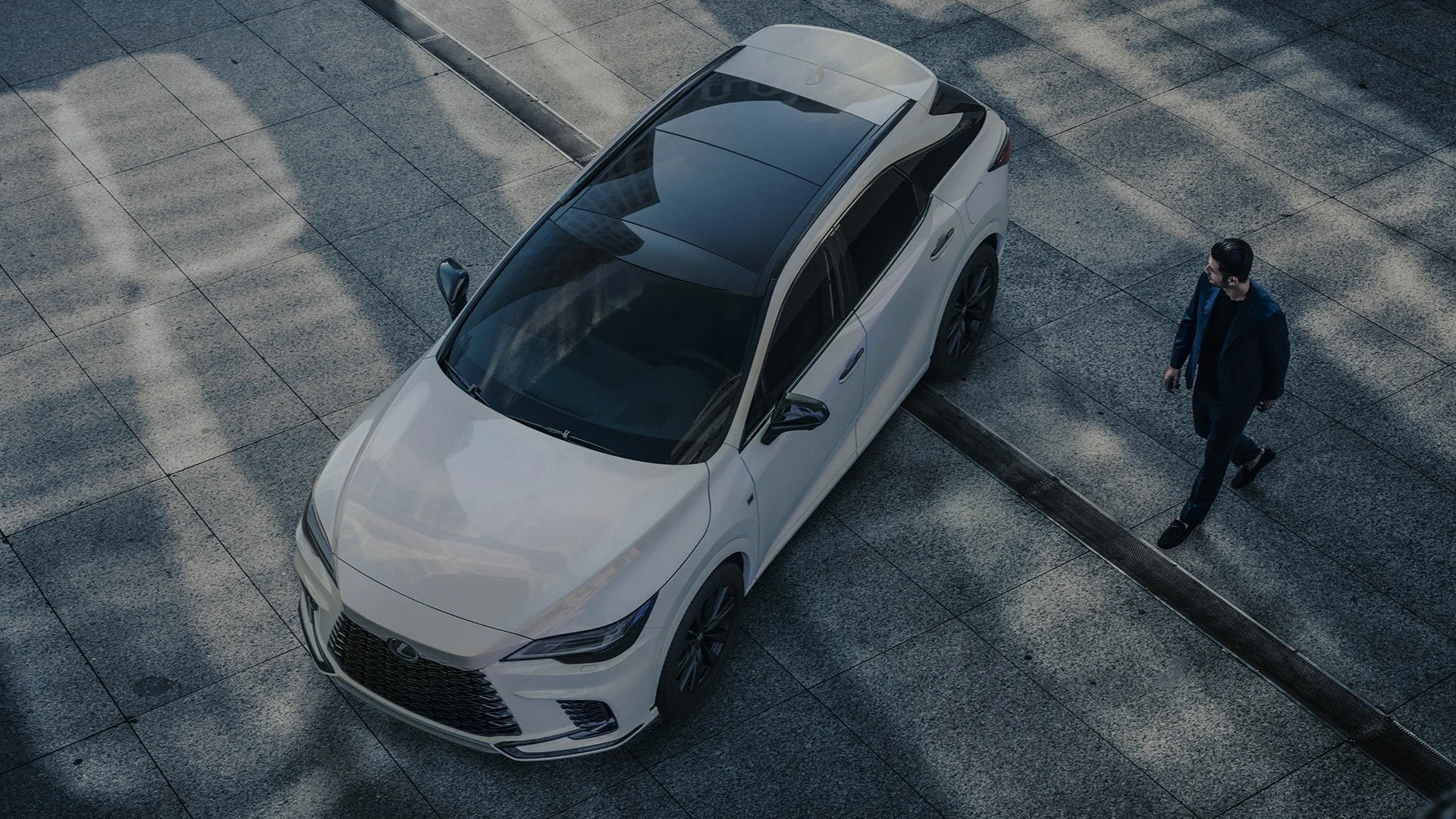 An overhead view of a white Lexus RX with a black roof as its driver walks toward it