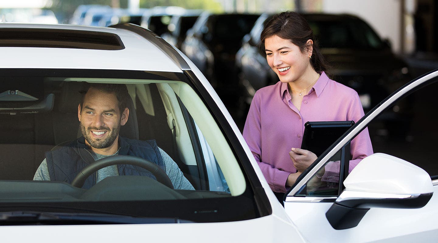 Lexus service advisor with a tablet talking to a customer sitting in the driver's seat