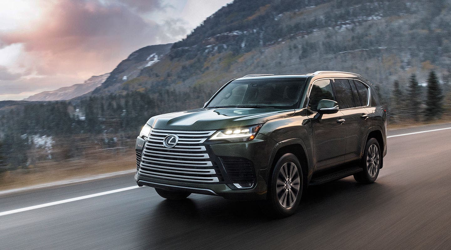 Lexus LX in dark green on a mountain road below a snow-dusted ridge