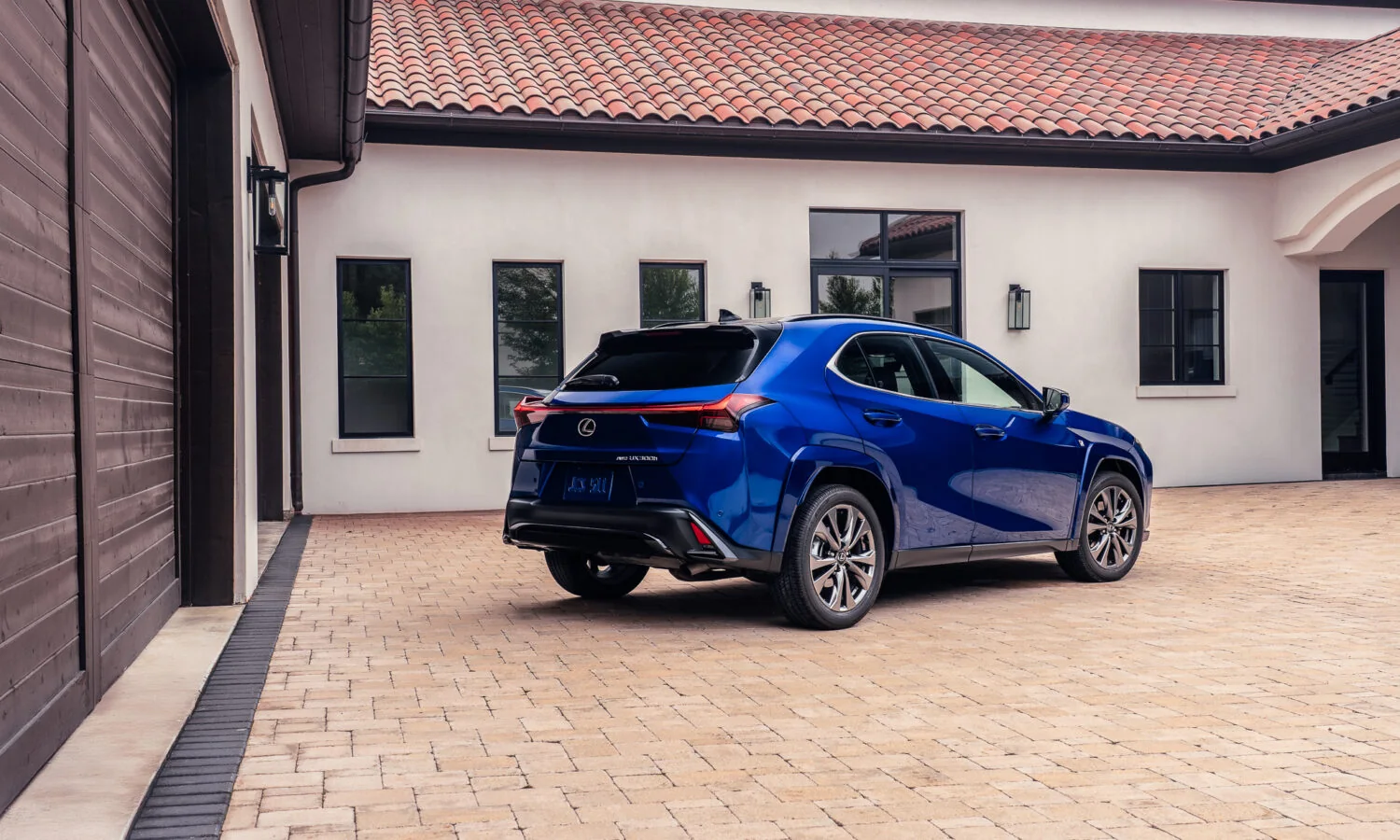 Lexus UX 300h F SPORT in blue, rear three-quarter view alongside the house