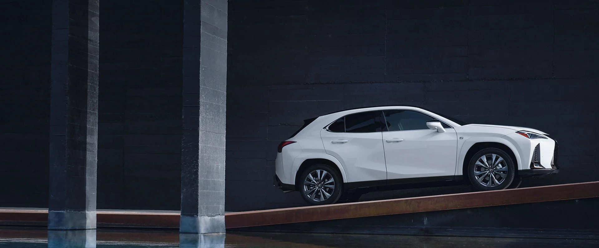 A white Lexus UX in side profile, parked in a dark covered arcade between concrete pillars