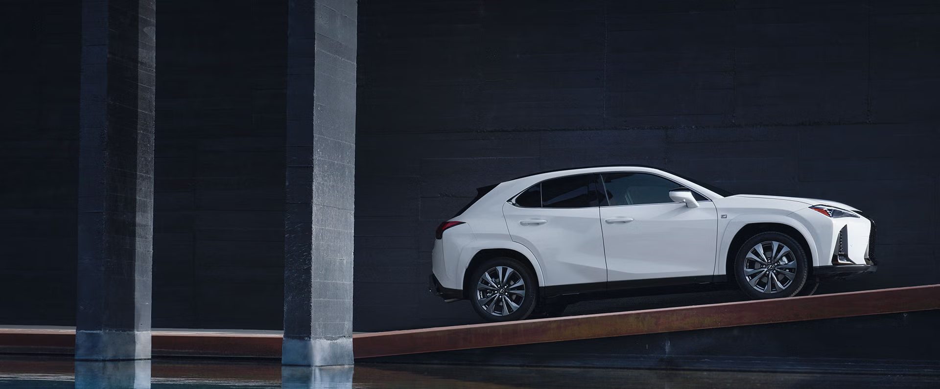 Lexus UX in white, side view, on a ramp against a dark concrete wall